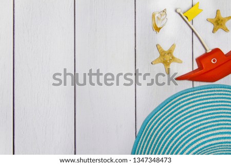 Concept of travel - toy boat, hat, various exotic shells and other sea treasures on a light wooden background with sand view from the top.