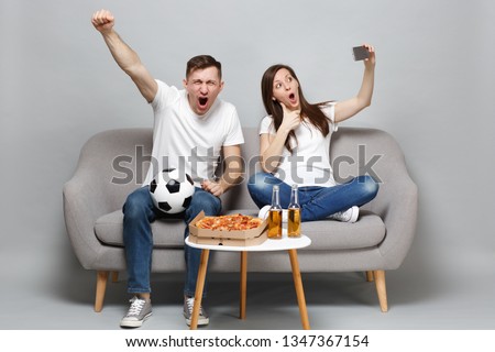 Fun couple woman man football fans cheer up support favorite team, expressive gesticulating hands, showing thumb up doing selfie shot on mobile phone isolated on grey background. Sport family concept