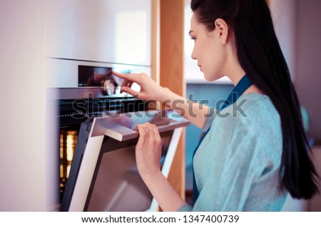 Beautiful young woman checking how her cake is doing in the oven