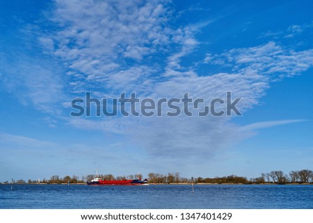 scenic background picture with a blue and red coaster on the river Weser (Germany) under vivid blue sky with white clouds in bright sunlight