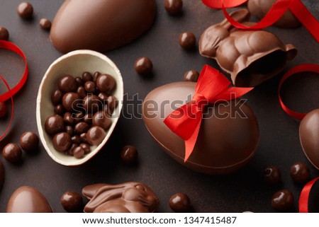 Easter composition with chocolate eggs and bunnies decorated with red ribbon on dark brown background, holiday concept
