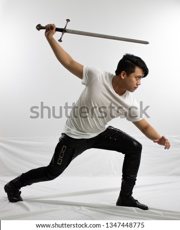 Man in black leather pants and white shirt posing with sword Royalty-Free Stock Photo #1347448775