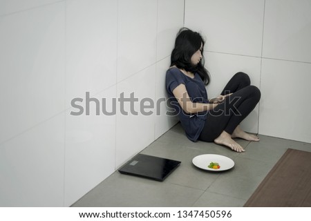 Picture of anorexia woman sitting with a plate of salad and weight scales in the bathroom
