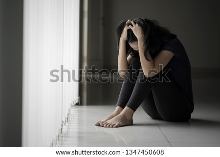 Picture of a desperate woman scratching her head while sitting near the window in black background Royalty-Free Stock Photo #1347450608