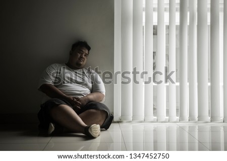 Picture of lonely fat man looks daydream while sitting near the window in the dark room