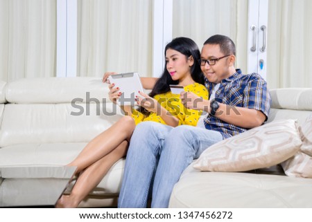 Picture of young couple shopping online by using a digital tablet while sitting on the couch. Shot at home