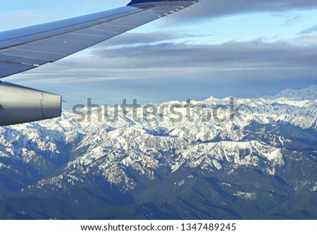 Wide aerial shot of Colorado with snow-capped mountains in the distance, with an airplane wing seen in picture. 