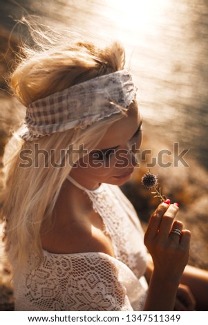 portrait of blond hair woman siting on the dry flowers slope and enjoing calm and silence, wearing in boho style closeses against the sea or ocean