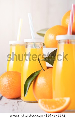 Glass bottles of organic fresh orange juice with raw oranges in white wooden box