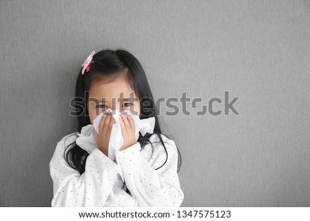 Asian child or kid girl sick and sad with sneezing on nose and cold cough on tissue paper because influenza and weak or virus bacteria from dust weather or smoke and kindergarten school for medical Royalty-Free Stock Photo #1347575123