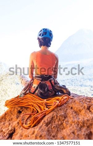 Climber sits near the rope and prepares to overcome the route. Slender girl holds climbing equipment. A woman in a helmet on the background of beautiful mountains. Rest after climbing.
