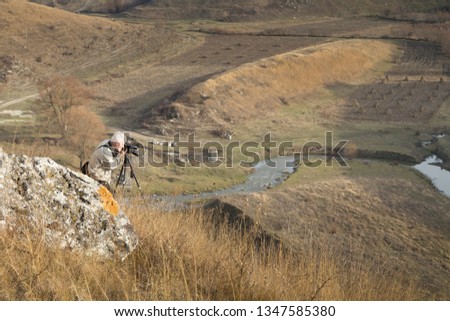 The photographer is doing a landscape shooting. He is located above the river.