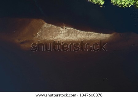 Top view of the sandy islands with green bushes and grass against the background of dark water. The shallows at the bottom of the river. Abstract landscape with drone