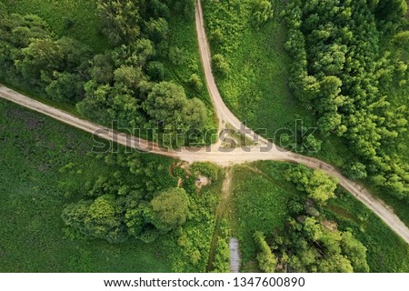 Top view of the dirt road with a crossroads and dense green forests. Beautiful bright landscape photography with drone on a summer day Royalty-Free Stock Photo #1347600890