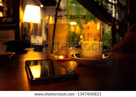 Picture of An Orange Cheesecake with A glass of Lime Juice as complement and A phone on a table
