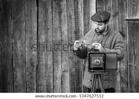 Photographer prepares for shooting and inserts film holder into retro large format camera. Concept - photography of the 1930s-1950s, monochrome effect