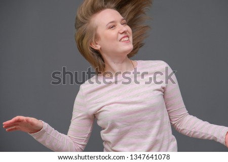 portrait of soncept young cheerful long-haired brunette woman standing in casual clothes, shaking hair and talking. It is standing on a gray background and shows different emotions.