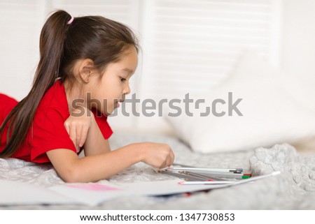 cute little child girl in red pajamas draws with pencils at home