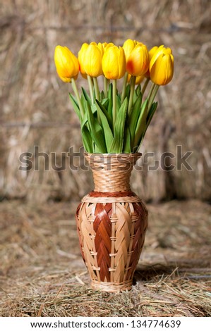 Yellow tulips in a wicker vase on background of hay.