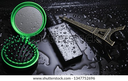 Bottle of perfume, statuette of the eyuylevaya tower, hairbrush mirror with water drops on a black background. Fashionable accessories. Product photo
