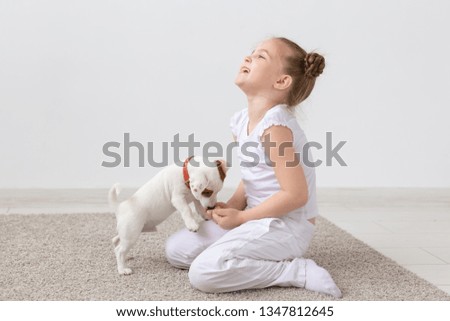 Animals, children and pets concept - little child girl sitting on the floor with cute puppy and playing