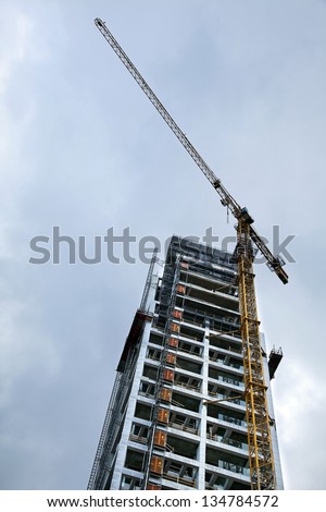 Low angle shot of a high rise residential building in the middle of construction, on the background of overcast gray skies.
