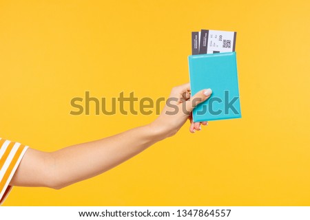 Close-up shot of woman's hand holding passport with flight tickets or boarding pass isolated on yellow background Royalty-Free Stock Photo #1347864557