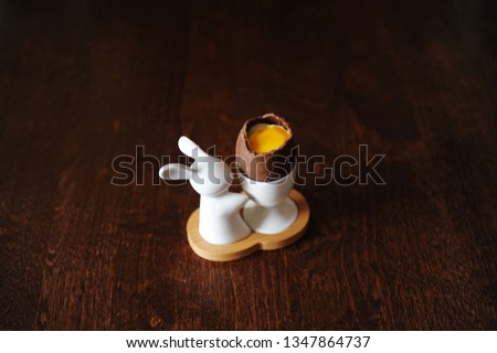 Easter dessert chocolate egg with cream imitating white and yolk. Holder with bunny. Wooden background, free space