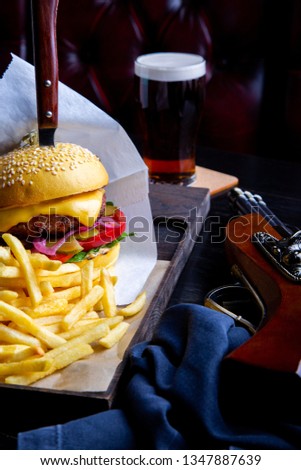 Craft beef burger and french fries on table in restaurant with glass of beer on dark background. Modern fast food lunch frame