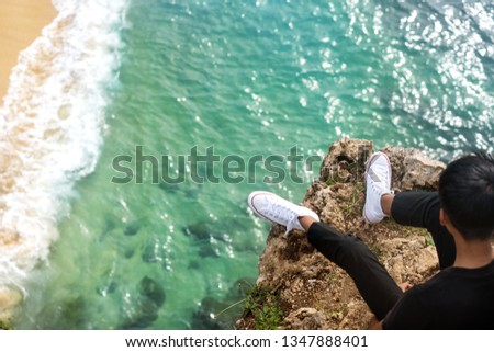 guy is sitting on a rock by the ocean