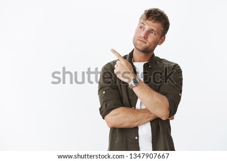 Not bad at all. Portrait of impressed handsome male customer doing shopping tlting head curiously as pointing and looking left with interest as seeing cool thing, posing over gray background