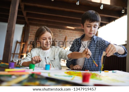 Portrait of two happy children, brother and sister painting picture together, copy space