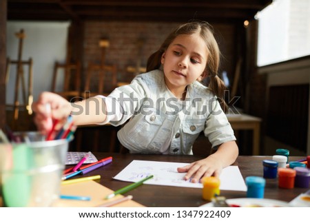 Portrait of cute little girl painting pictures in art class or at home, copy space