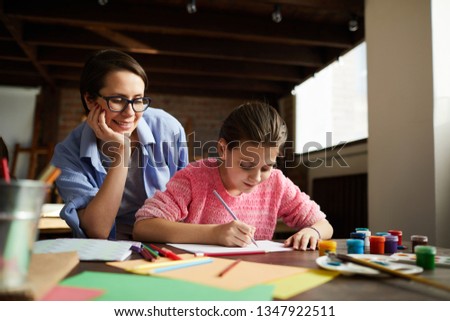 Portrait of smiling young woman watching girl drawing picture in art class, copy space