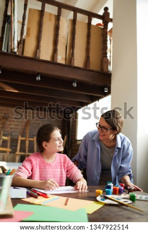 Portrait of smiling young woman watching teenage girl painting picture in art class, copy space