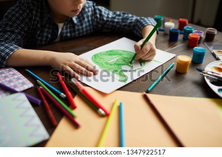 Cropped portrait of little boy drawing picture of green monster in art class, copy space