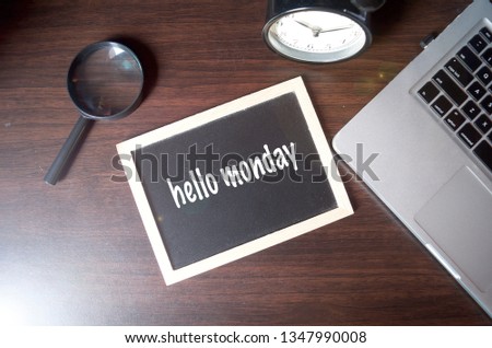 Blackboard writing "hello monday" on wooden desk background with laptop, magnifying and alarm clock. Conceptual image. Selective focus.