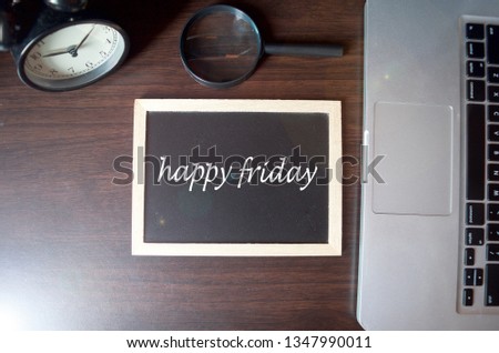 Blackboard writing "happy friday" on wooden desk background with laptop, magnifying and alarm clock. Conceptual image. Selective focus.