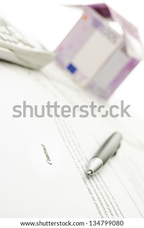 Pen on a contract of house sale with house made of 500 Euro money in background.