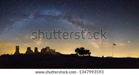 Panoramic shot of a medieval castle ruin on a clear night. The Milky Way arch is visible in the background.