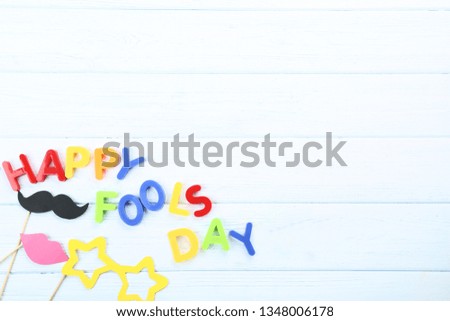 Inscription Happy Fool's Day by colorful letters with paper fish and booth props on wooden table