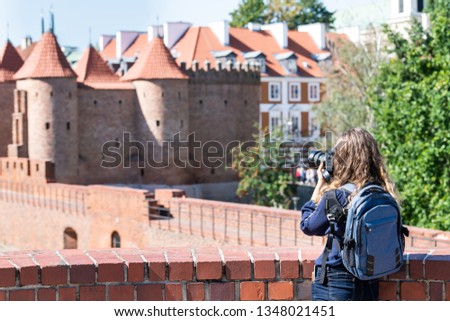 Warsaw, Poland Famous Barbican old town historic city during summer day and red orange brick wall fortress architecture with young woman travel tourist backpack taking picture with camera