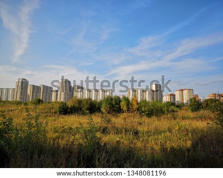 View of the sleeping area of the city with colored multi-storey houses standing at the other end of the field overgrown with tall yellow grass Royalty-Free Stock Photo #1348081196