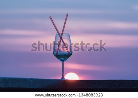 drinking glass with two straws, over an orange and teal   sunset  background, ROMANTIC CONCEPT