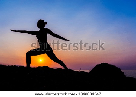 Silhouette of a young woman doing yoga on the beach at sunset.