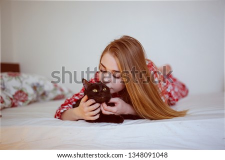Beautiful girl with a cat on a bed in pajamas, light background and toning, soft focus