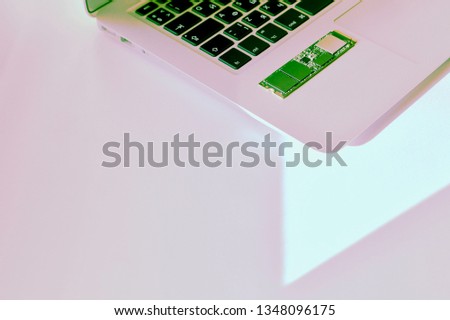 A fragment of a laptop keyboard and green SSD-drive. Buttons with Russian-English characters. On the surface in a light-lilac shade and a light-colored white corner.