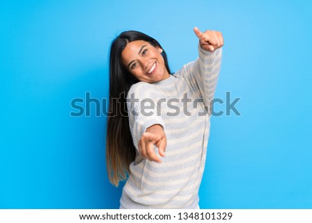 Young Colombian girl with sweater points finger at you while smiling