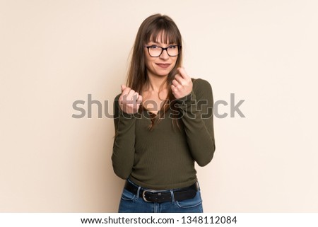 Young woman on ocher background making money gesture
