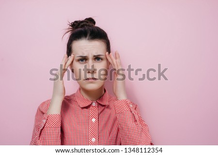 Young tired brunette woman wears red shirt, keeps finger on temples, suffers from headache, feels pain, being overworked, need rest and calm. People, tiredness, exhaustion concept